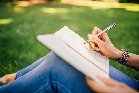 Eine Person, die draußen im Grünen sitzt und in ein Notizbuch schreibt